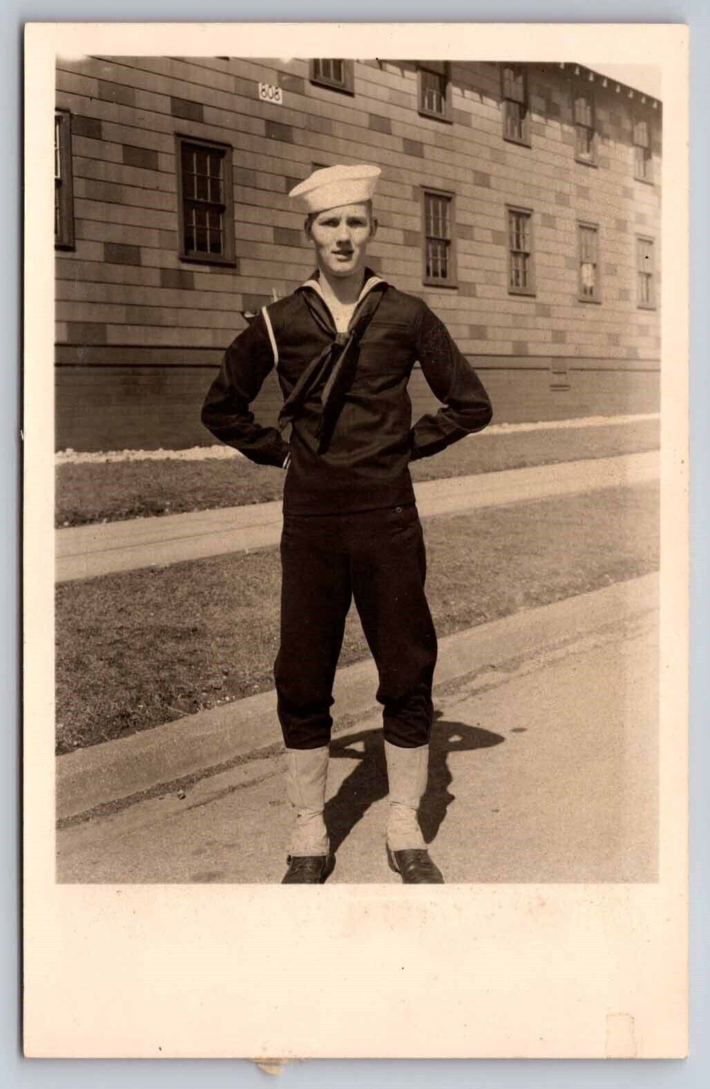eStampsNet - RPPC WWII Sailor in Uniform Standing in Front of Barracks Postcard